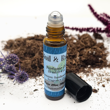 Load image into Gallery viewer, Roll-on perfume bottle with a blue label on a white background with soil and plants.