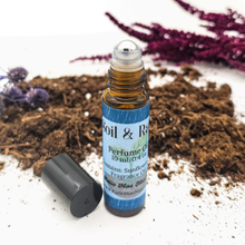 Load image into Gallery viewer, Roll-on perfume bottle labeled 'Soil & Rain' with purple flowers and soil in the background