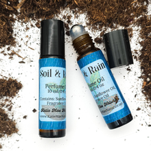 Load image into Gallery viewer, Two small bottles of 'Soil & Rain' perfume and rollerball oil on a textured surface.
