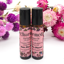 Load image into Gallery viewer, Two bottles of 'Charmed' perfume oil with pink labels against a floral background.