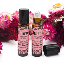 Load image into Gallery viewer, Two bottles of 'Charm' perfume oil with pink labels on a white background with flowers.