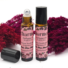 Load image into Gallery viewer, Two bottles of 'Charm' perfume oil with pink labels on a white background with purple flowers.