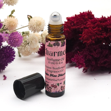 Load image into Gallery viewer, Perfume oil bottle with pink label surrounded by flowers on a white background