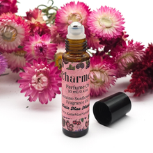Load image into Gallery viewer, Perfume oil bottle with pink label surrounded by pink flowers on a white background