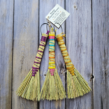 Load image into Gallery viewer, Three colorful brooms on a wooden surface with a tag above them.
