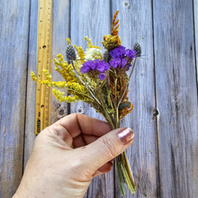 Load image into Gallery viewer, Hand holding a bouquet of purple and yellow flowers against a wooden background with a ruler for scale.
