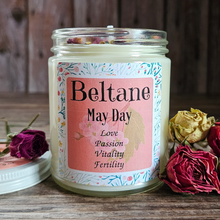 Load image into Gallery viewer, Candle jar with 'Beltane May Day' label surrounded by dried roses on a wooden surface
